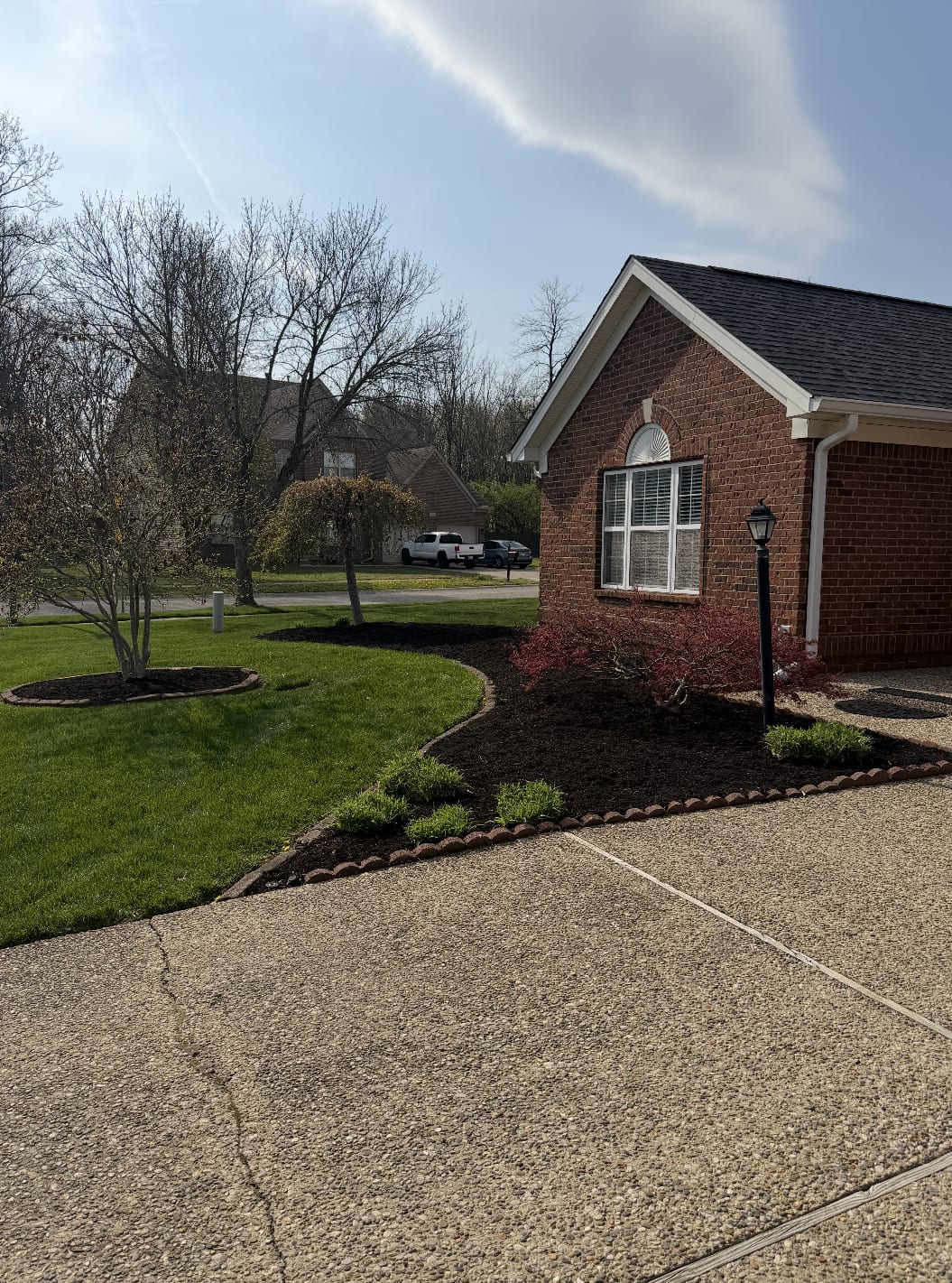 Front-yard mulch refresh with ornamental plantings against a red-brick home